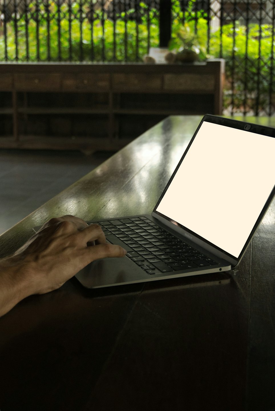Dłoń pisze na srebrnym laptopie na drewnianym stole.